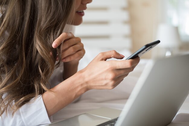 Felice bella donna che lavora su un computer portatile sul letto in casa