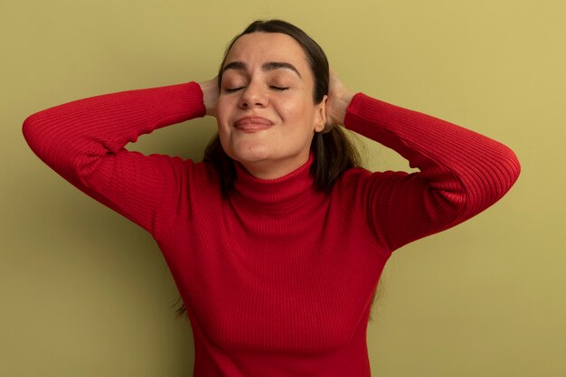 Felice bella donna sta con gli occhi chiusi tenendo la testa isolata sulla parete verde oliva