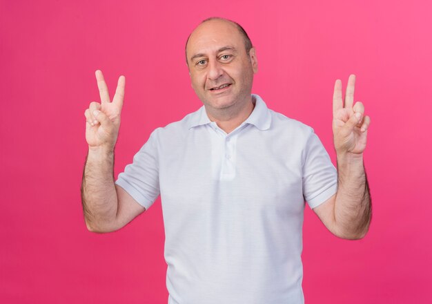 Felice casual uomo d'affari maturo facendo segni di pace facendo segni di pace isolati su sfondo rosa