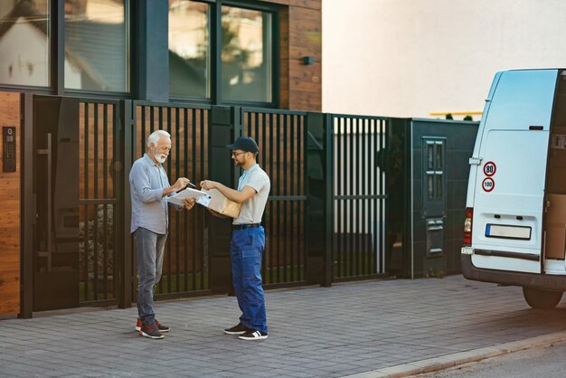 Felice cliente senior che firma a un corriere per la consegna a domicilio