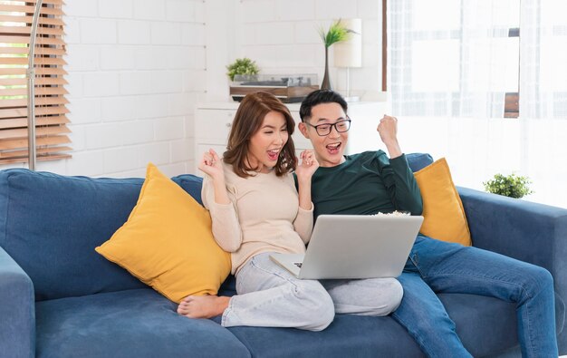 Felice coppia asiatica uomo e donna sta trascorrendo il fine settimana insieme guardando film sul divano in casa, rilassandosi e godendosi il popcorn.