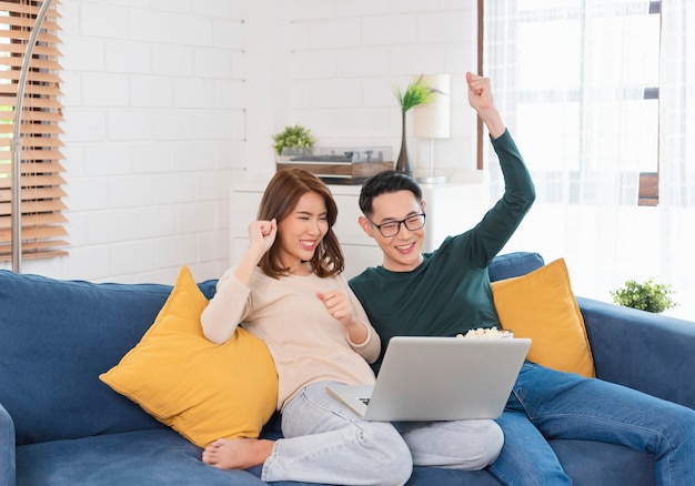 Felice coppia asiatica uomo e donna sta trascorrendo il fine settimana insieme guardando film sul divano in casa, rilassandosi e godendosi il popcorn.