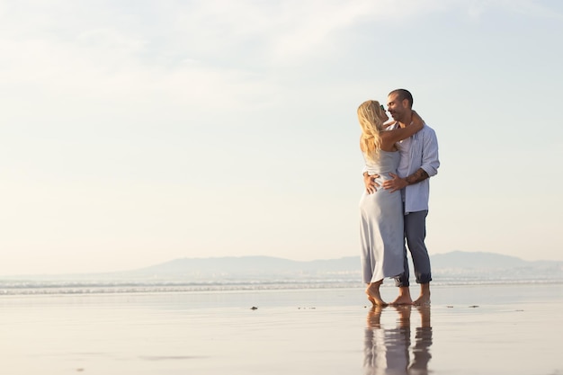 Felice coppia maschile e femminile che trascorre del tempo in spiaggia. Marito e moglie in abiti casual che si abbracciano il giorno d'estate. Vacanza, felicità, concetto di relazione