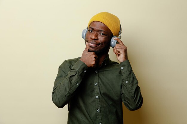 felice di mostrare i pollici in su giovane maschio afroamericano con cappello e cuffie che indossa una camicia verde isolata su sfondo bianco