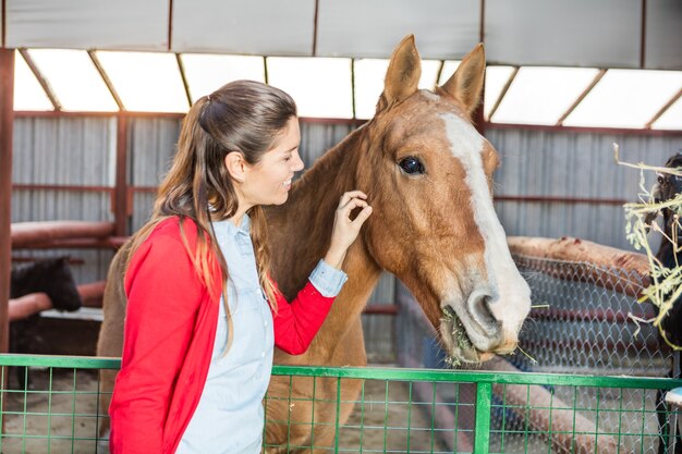 Felice donna accarezzando il cavallo nella stalla