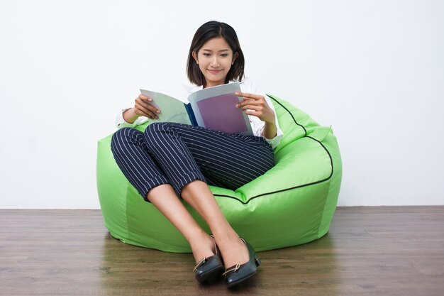 Felice donna asiatica lettura rivista sul beanbag