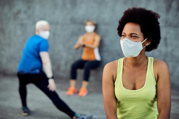 Felice donna atletica nera che indossa una maschera facciale mentre si riscalda all'aperto