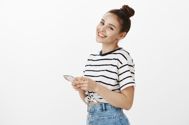 Felice donna attraente in piedi con il telefono cellulare e sorridente