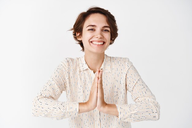 Felice donna candida dice grazie e sorride, tenendosi per mano in namaste, prega il gesto e sembra grato, in piedi sul muro bianco