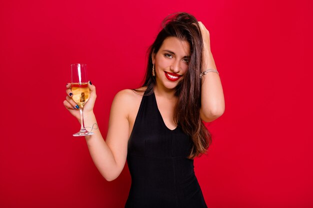 Felice donna che balla e tiene champagne. Foto interna di una bella signora con lunghi capelli castani che si diverte a una festa con un'espressione del viso soddisfatta