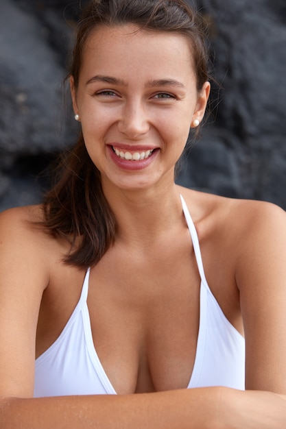 Felice donna con un sorriso a trentadue denti, seno perfetto, guarda volentieri, vestita in costume da bagno