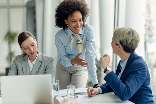 Felice donna d'affari afroamericana che parla con colleghe mentre lavora in ufficio