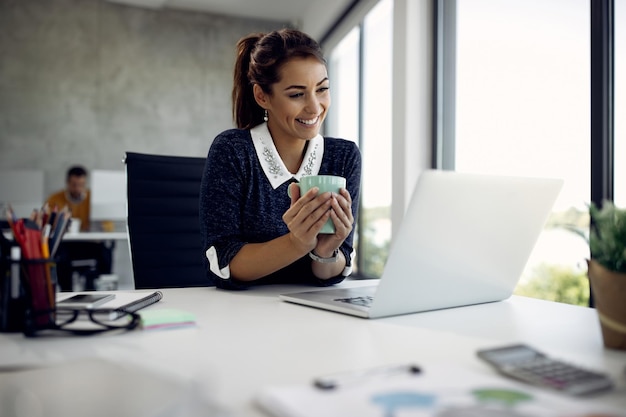 Felice donna d'affari che effettua una videochiamata sul laptop durante la sua pausa caffè in ufficio