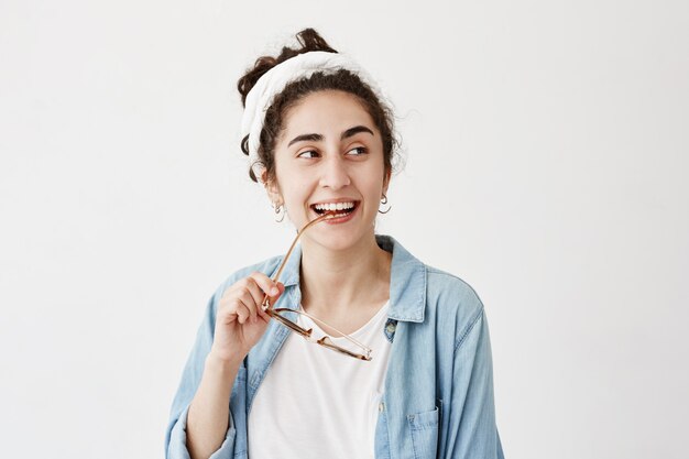 Felice donna dai capelli scuri e sorridente in doppio panno in camicia di jeans, con occhiali da sole, ha buon umore dopo aver ricevuto una buona notizia, felice di incontrare amici e parenti. Persone, felicità, concetto di espressioni facciali