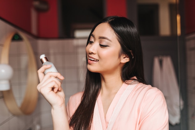 Felice donna dai capelli scuri guarda crema per il viso e sorride