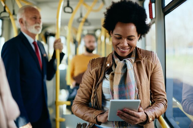 Felice donna di colore che utilizza tablet digitale durante il pendolarismo in autobus