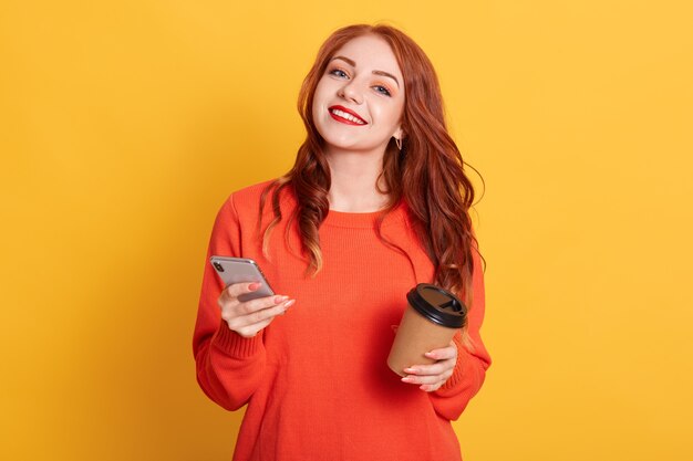 Felice donna europea vestita di casual maglione arancione, pose, guarda sorridendo alla telecamera