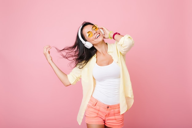 Felice donna latina con i capelli neri che ondeggia ballando e sognando qualcosa. Donna allegra in accessori colorati, godersi la musica e sorridere