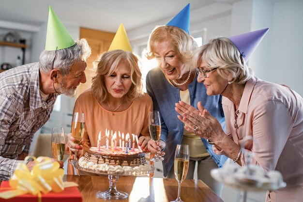 Felice donna matura che soffia le candeline di compleanno su una torta mentre festeggia con gli amici a casa