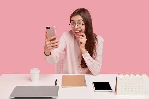 Felice donna positiva tiene il cellulare davanti al viso, effettua una videochiamata, è connessa a Internet wireless, indossa una camicia formale