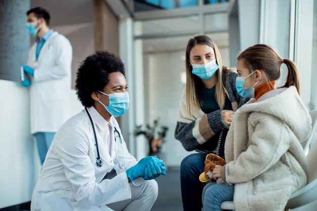 Felice dottoressa afroamericana che parla con madre e figlia nella sala d'attesa della clinica medica