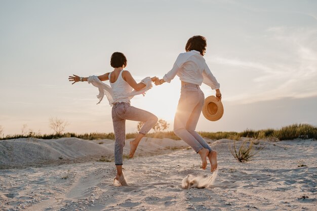 Felice due giovani donne divertendosi sulla spiaggia al tramonto, romanticismo gay amore lesbico