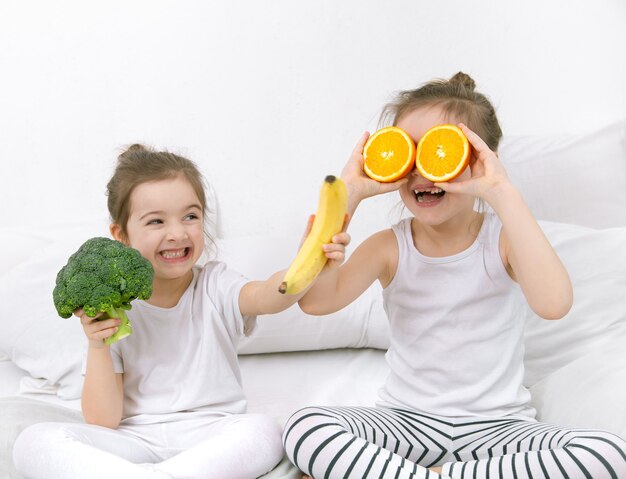 Felice due simpatici bambini giocano con frutta e verdura su uno sfondo chiaro. Cibo sano per i bambini.