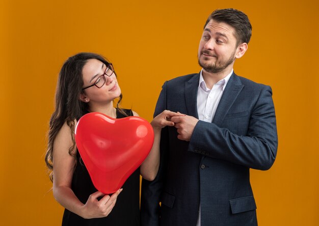 Felice e bella coppia uomo e donna con palloncino rosso a forma di cuore che si guardano per celebrare il giorno di san valentino