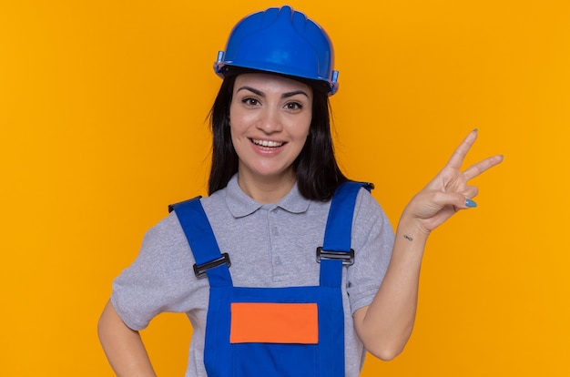 Felice e positiva giovane donna costruttore in uniforme da costruzione e casco di sicurezza