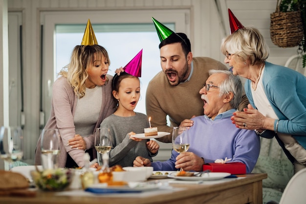 Felice famiglia allargata che soffia una candela di compleanno su una torta mentre si festeggia nella sala da pranzo