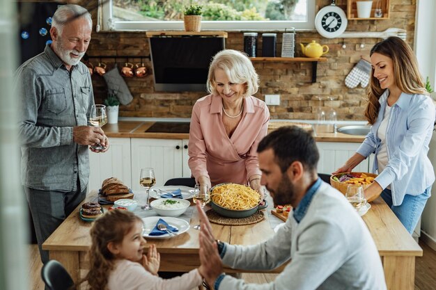 Felice famiglia allargata godendo in un pranzo di famiglia a casa Focus è su una donna matura che serve cibo al tavolo