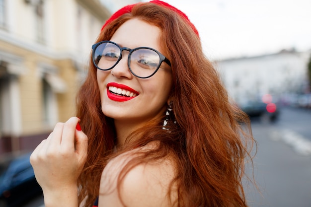 Felice favolosa donna allo zenzero in elegante berretto rosso in strada