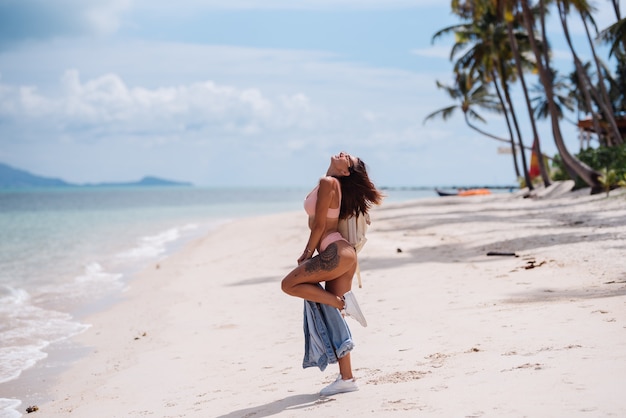 Felice fit donna tatuata sportiva abbastanza abbronzata sulla spiaggia con giacca di jeans