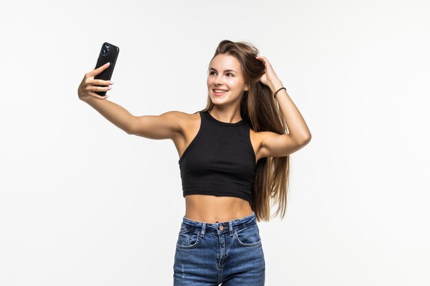 Felice flirtare ragazza che scatta foto di se stessa tramite il telefono, su bianco