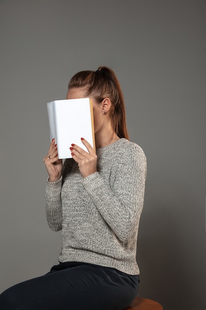 Felice giornata mondiale del libro e del diritto d'autore, leggi per diventare qualcun altro - donna che copre il viso con il libro mentre legge sul muro grigio.