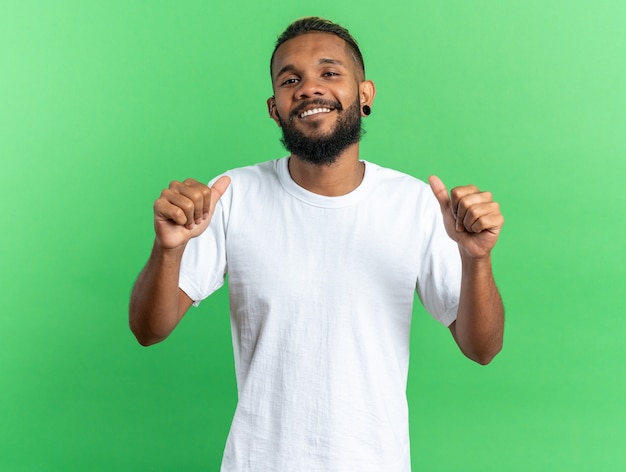 Felice giovane afroamericano in maglietta bianca sorridente fiducioso che indica se stesso in piedi sopra il verde