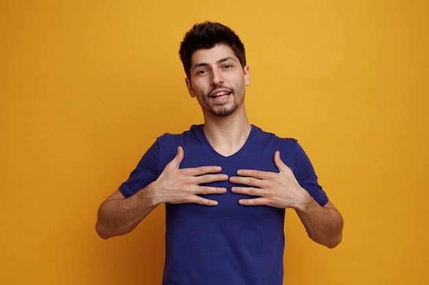 Felice giovane bell'uomo che tiene le mani sul petto guardando la fotocamera su sfondo giallo