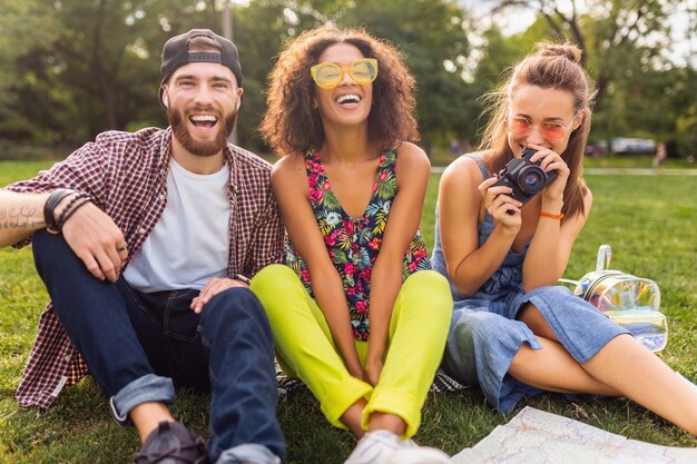 Felice giovane compagnia di amici seduti nel parco che viaggiano guardando nella mappa visite turistiche, uomini e donne che si divertono insieme