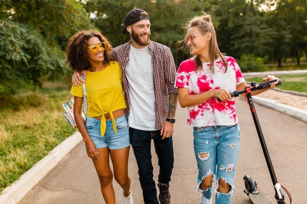 Felice giovane compagnia di amici sorridenti che camminano nel parco con scooter elettrico, uomini e donne che si divertono insieme