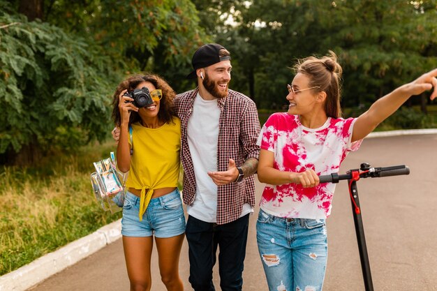 Felice giovane compagnia di amici sorridenti che camminano nel parco con scooter elettrico, uomini e donne che si divertono insieme