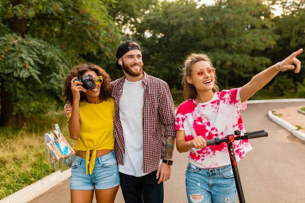 Felice giovane compagnia di amici sorridenti che camminano nel parco con scooter elettrico, uomini e donne che si divertono insieme