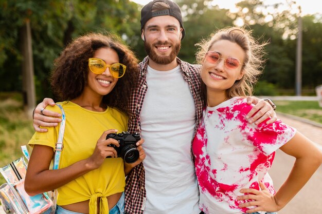 Felice giovane compagnia di amici sorridenti emotivi che camminano nel parco con macchina fotografica, uomini e donne che si divertono insieme