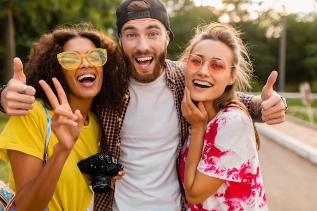 Felice giovane compagnia di amici sorridenti emotivi che camminano nel parco con macchina fotografica, uomini e donne che si divertono insieme