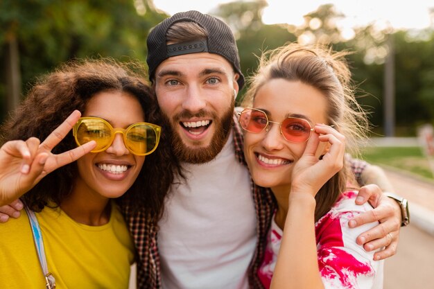 Felice giovane compagnia di amici sorridenti emotivi che camminano nel parco con macchina fotografica, uomini e donne che si divertono insieme