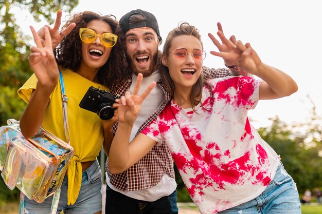 Felice giovane compagnia di amici sorridenti emotivi che camminano nel parco con macchina fotografica, uomini e donne che si divertono insieme