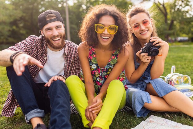 Felice giovane compagnia di parlare sorridenti amici seduti nel parco, uomo e donna che si divertono insieme, viaggiando con la macchina fotografica