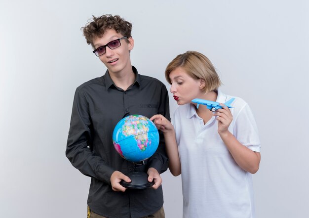 Felice giovane coppia di turisti uomo e donna che tiene globo e aereo giocattolo in piedi insieme sul muro bianco