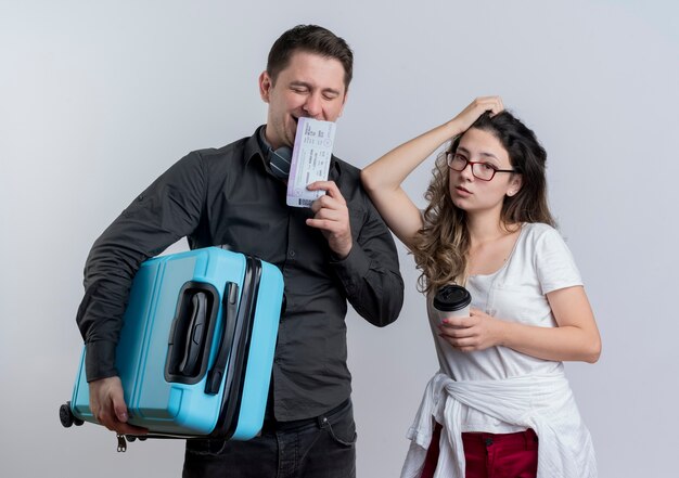 Felice giovane coppia di turisti uomo e donna che tiene la valigia e biglietti aerei in piedi sopra il muro bianco