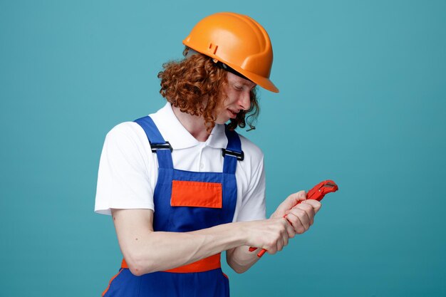 Felice giovane costruttore in uniforme tenendo la chiave a gas isolata su sfondo blu