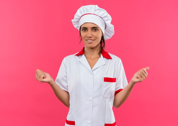 Felice giovane cuoco femminile che indossa l'uniforme dello chef che mostra sì gesto con lo spazio della copia